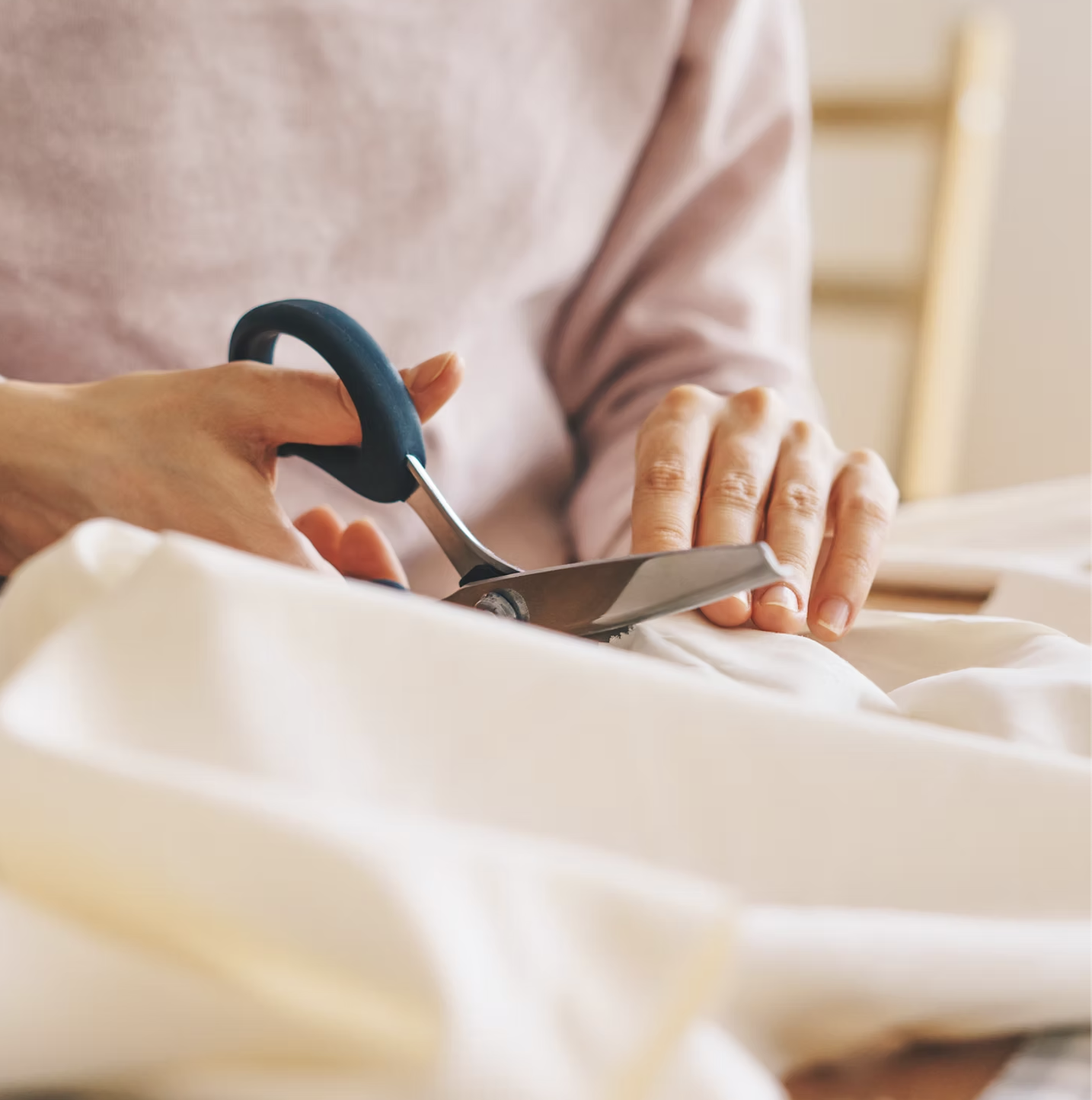 Hands cutting fabric with tailoring scissors on a worktable